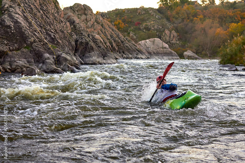Man in green kayak fights with rapids of fast mountain river among the rocks. Whitewater kayaking, extreme water sport.