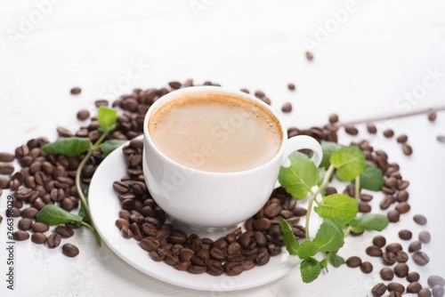 white cup of coffee on a background of scattered coffee beans on a white background