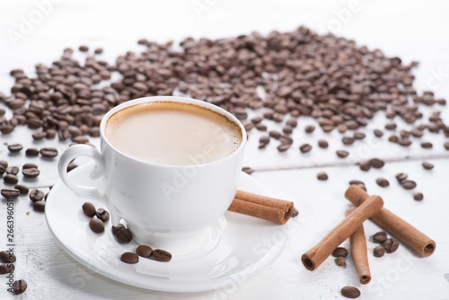 white cup of coffee on a background of scattered coffee beans on a white background