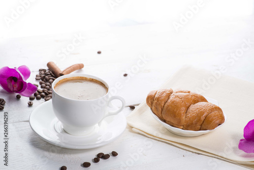 cup of coffee and a croissant on a served table with flower buds