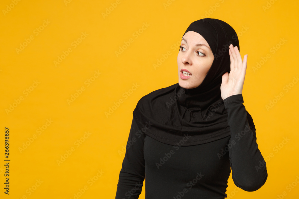 Sad crying confused young arabian muslim woman in hijab black clothes try to hear you isolated on yellow wall background, studio portrait. People religious Islam lifestyle concept. Mock up copy space. Sad crying confused young arabian muslim woman in hijab black clothes try to hear you isolated on yellow wall background, studio portrait. People religious Islam lifestyle concept. Mock up copy space.
