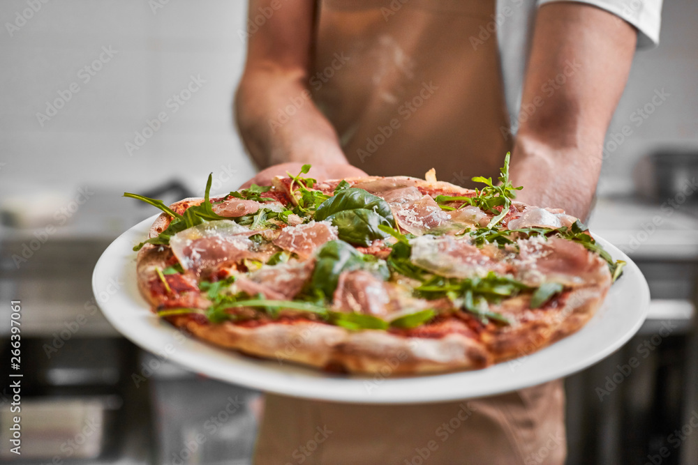 Close up of pizza held by chef at pizzeria kitchen