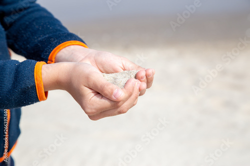 a little boy slowly lets sand flow through his hands scattered by the wind. © DEWI-Stockphotos