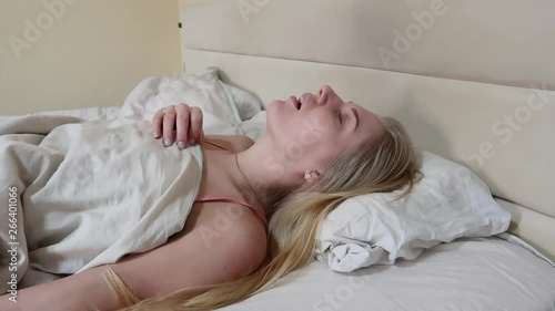 young attractive blonde sleeps on her back with her mouth open, closes her mouth and turns her head to the side, snoring concept