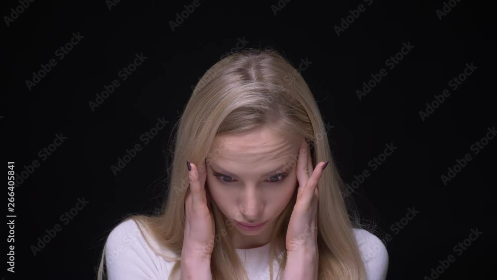 Closeup portrait of young pretty blonde female having a headache and being tired with background isolated on black Closeup portrait of young pretty blonde female having a headache and being tired with background isolated on black
