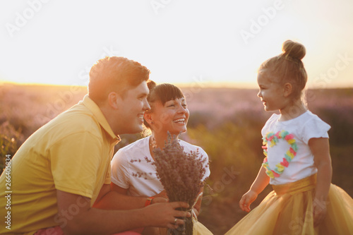 Young family in yellow clothes walk on purple lavender flower meadow field background, have fun, play with little cute child baby girl. Mother father, small kid daughter. Outdoors summer day concept.