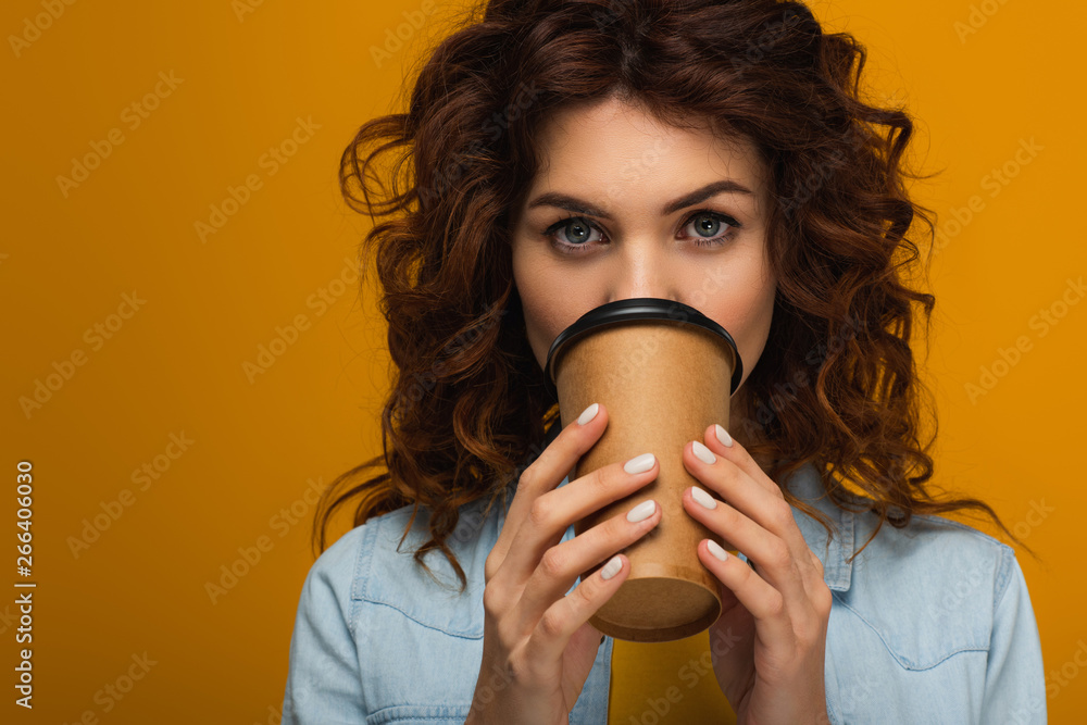 curly redhead woman covering face with paper cup while drinking isolated on orange curly redhead woman covering face with paper cup while drinking isolated on orange