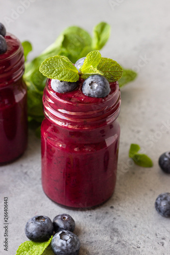 Delicious blueberry smoothie with fresh berries and mint in glass jars. Summer healthy drink. Grey stone background. Copy space.