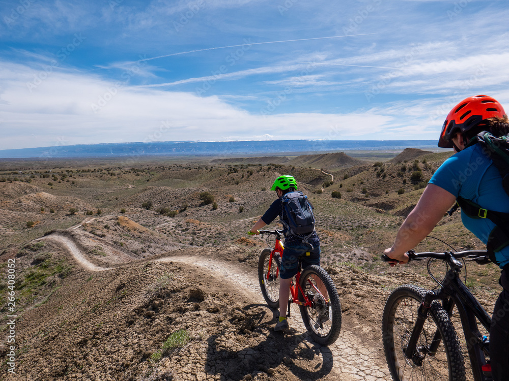 A little boy mountain bikes on singletrack trail with his mother A little boy mountain bikes on singletrack trail with his mother