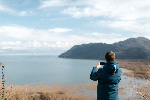 A boy by the lake is taking a picture with phone camera photo