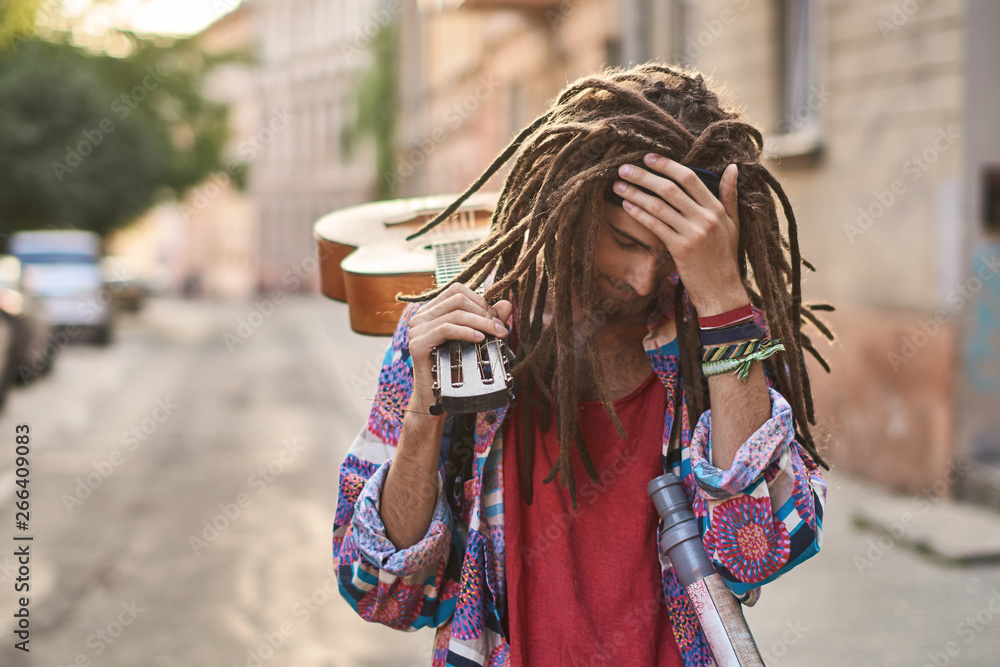 Young handsome bearded man hippie with dreadlocks looks depressed or dramatic