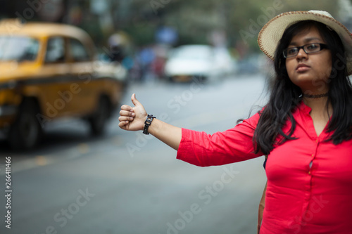 Young woman showing hand signal for hitchhiking in the busy street of a city photo