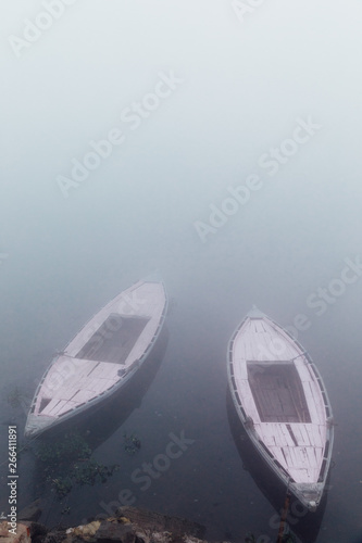 Pink boats in the water of the Ganges river during a densely foggy morning