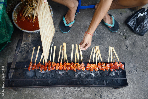 Hands grilling Indonesian pork satay over a small charcoal grill on the street photo