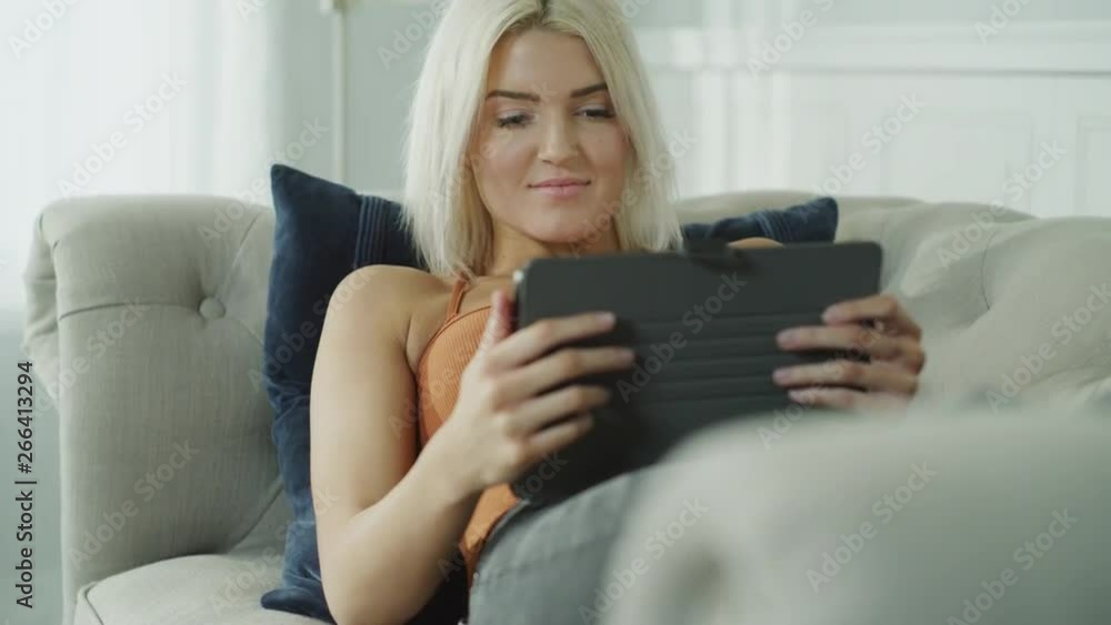 Tilt up to woman laying on sofa reading digital tablet / Cedar Hills, Utah, United States Tilt up to woman laying on sofa reading digital tablet / Cedar Hills, Utah, United States