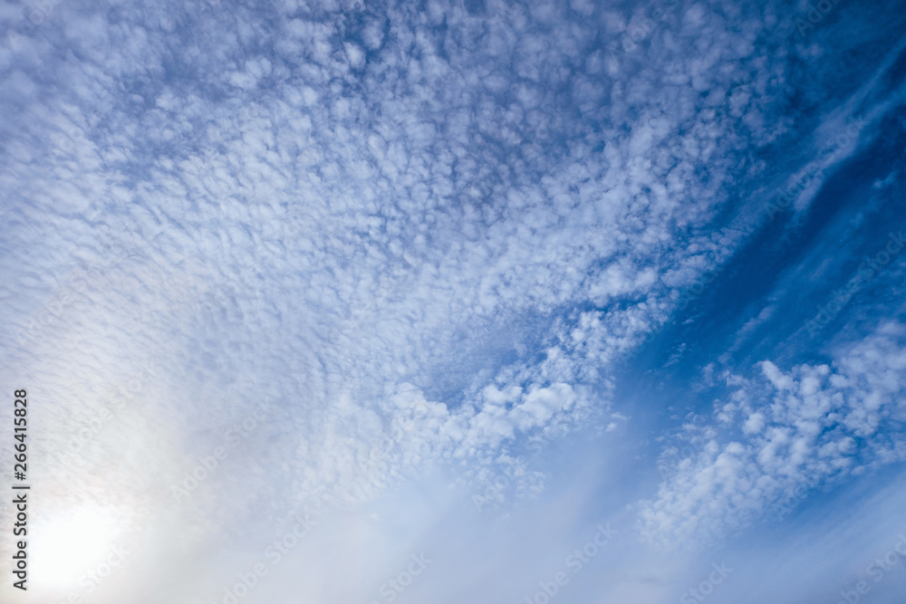 Light small cirrocumulus clouds on a bright sunny blue sky. Heavenly daylight background.