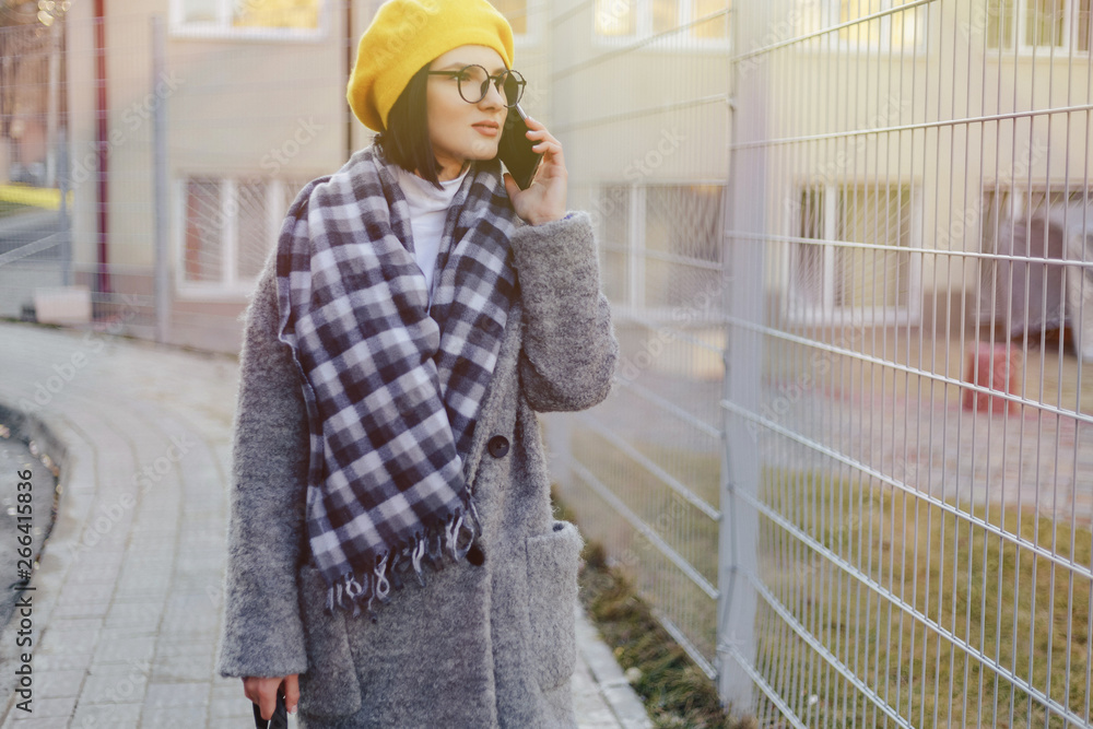 An attractive young girl wearing sunglasses in a coat walking down the street and talking on the phone and smiles An attractive young girl wearing sunglasses in a coat walking down the street and talking on the phone and smiles