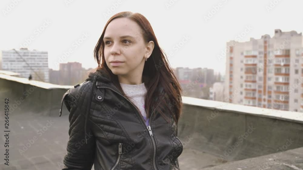 Woman in trendy jacket on roof edge. Portrait of young female in leather jacket, standing on the roof of at sunset Woman in trendy jacket on roof edge. Portrait of young female in leather jacket, standing on the roof of at sunset
