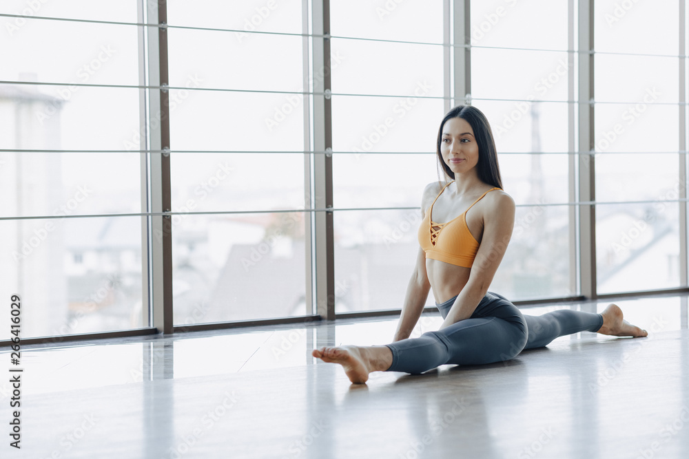 Fototapeta premium young attractive girl doing fitness exercises with yoga on the floor against the background of panoramic windows