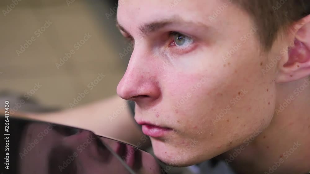 Close up of the face of a young master who repairs a car in a car repair shop, attentive, neat, reflective surface, aesthetic. Paintless dent repair Close up of the face of a young master who repairs a car in a car repair shop, attentive, neat, reflective surface, aesthetic. Paintless dent repair