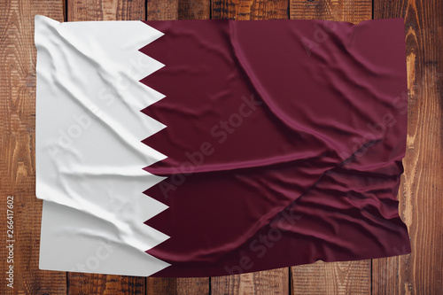 Flag of Qatar on a wooden table background. Wrinkled Qatari flag top view.