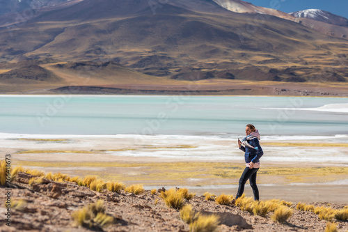 Landscape woman photographer taking mobile phone photos in an amazing wilderness environment at Atacama Desert Andes mountains lagoons. A woman cut out silhouette over the awe Tuyajto Lagoon scenery 