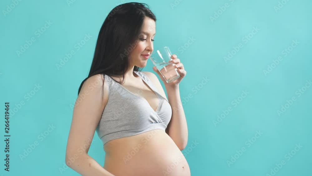 Young pregnant Caucasian model with long black hair drinks the purest water from a glass. Young pregnant Caucasian model with long black hair drinks the purest water from a glass.