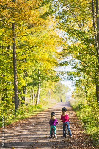 Two sisters ride bikes down a quiet country road; two children enjoy a fall bike ride