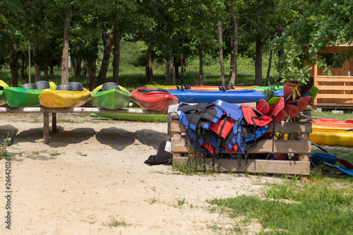 Obraz na płótnie Wypożyczalnia kajaków. Kolorowe kajaki poustawiane na stojakach leżą na plaży. Kapoki i wiosła poukładane w drewnianym pojemniku. w salonie