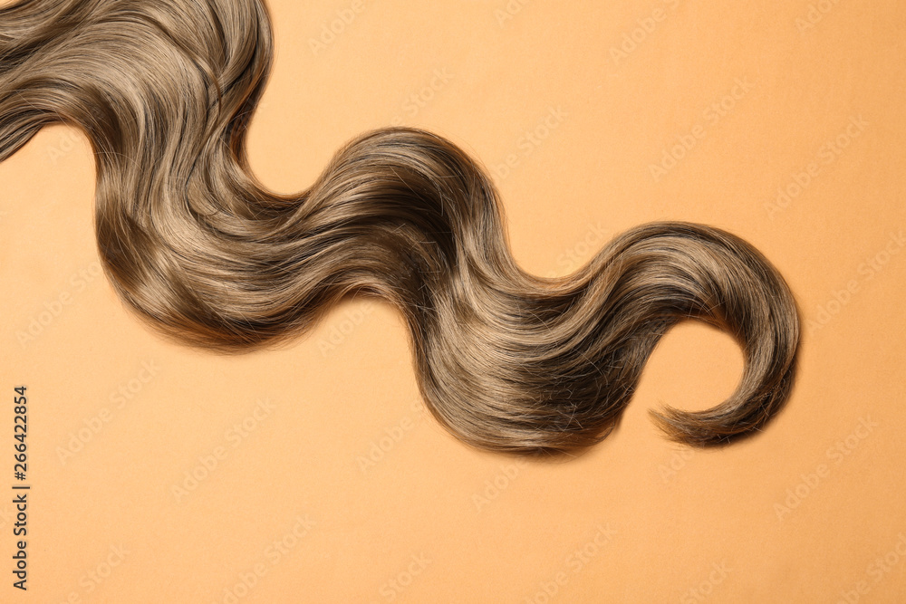 Lock of brown wavy hair on color background, top view Lock of brown wavy hair on color background, top view