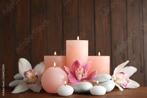 Photography Beautiful composition with candles, flowers and stones on table against wooden b