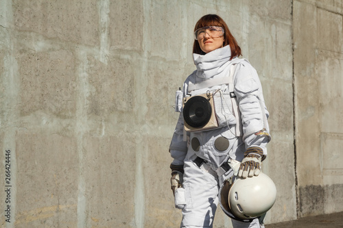 Beautiful girl astronaut without a helmet on the background of a gray wall. Fantastic space suit.