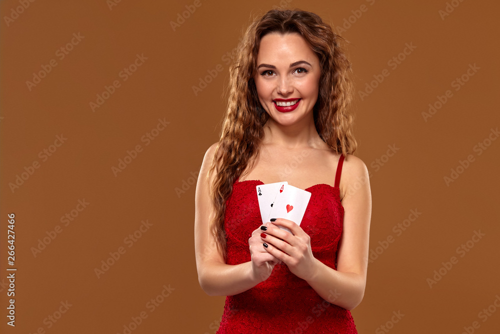 Pretty young brown-haired woman in red cocktail dress holding pair of aces and smiling Pretty young brown-haired woman in red cocktail dress holding pair of aces and smiling
