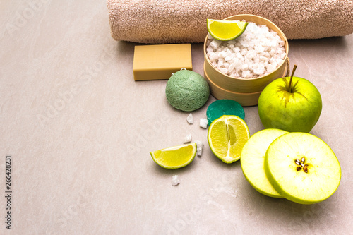 Spa concept, natural ingredients. Bath towel, sea salt with lime, apple, olive and mint soap, sponge. On a stone background