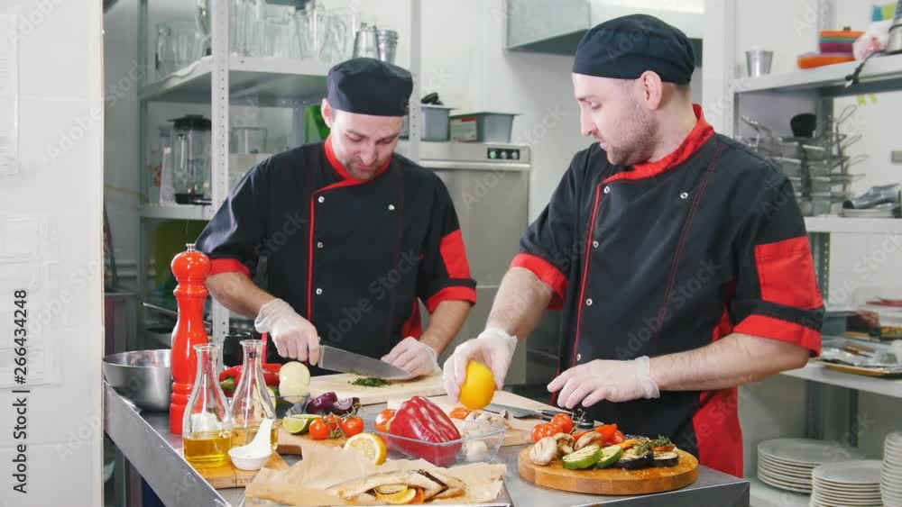 Restaurant kitchen. Two men working on serving dishes cutting lemon and greenery Restaurant kitchen. Two men working on serving dishes cutting lemon and greenery