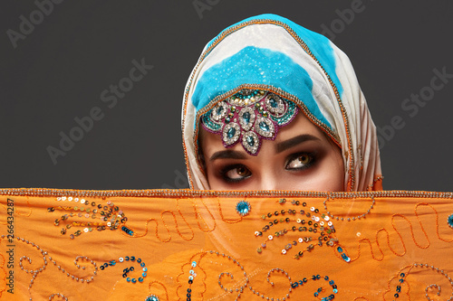 Studio shot of a chrming female wearing the colorful hijab decorated with sequins and jewelry. Arabic style. photo