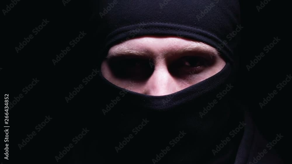 Dangerous bandit in balaclava turning to camera, isolated on dark background Dangerous bandit in balaclava turning to camera, isolated on dark background