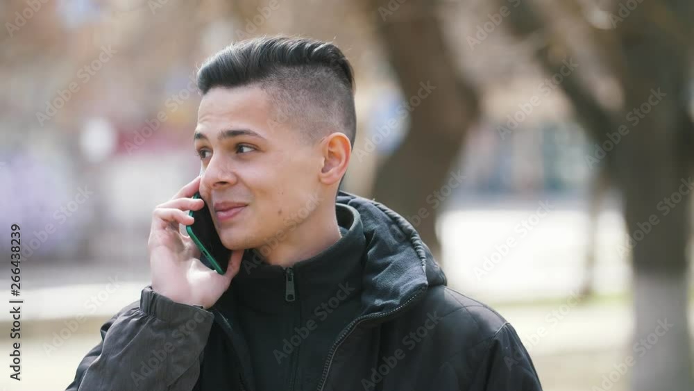 Joking young man speaking on the smartphone and smiling in an alley in spring Joking young man speaking on the smartphone and smiling in an alley in spring