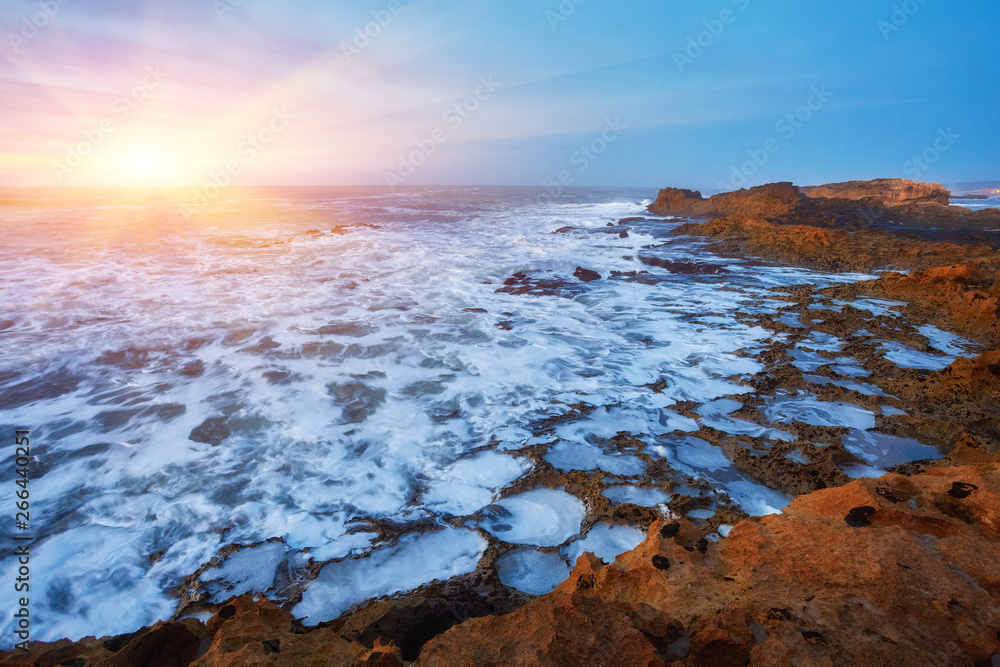 The stony coast of the Atlantic Ocean is washed by the waves during sunset, Essaouira