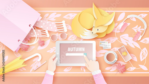 Women are using a digital tablet on autumn holiday with decorative fashion items and accessories on desk and cute pet fox take a rest on the desk. paper cut and craft style. vector, illustration.