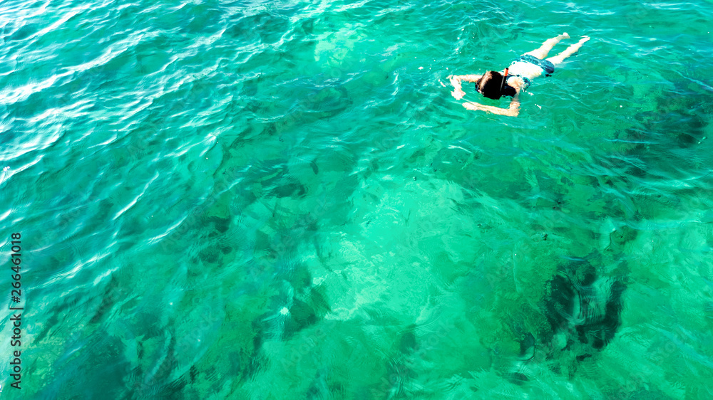 Aerial top view of woman snorkeling from above, girl snorkeler swimming in a clear tropical sea water with corals during summer vacation in Thailand