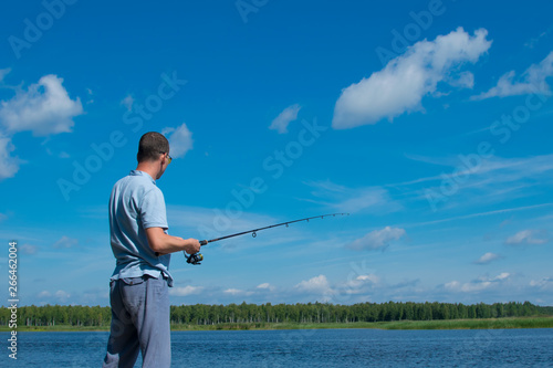 the man on the pier, in the yellow with glasses on the background of the lake, catches a fish