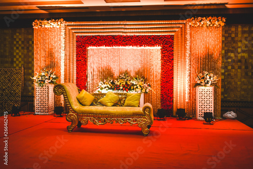 Huge stage at a wedding ceremony with beautiful yellow sofa for bride and groom. floral background lit by multiple stage lights.