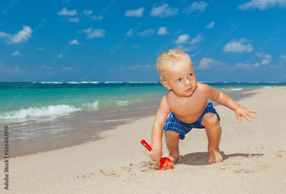 On sunny beach muddy happy baby boy play with fun, digging white sand before swimming in sea. Active children lifestyle, summer vacation travel with little kids at family resort on tropical islands. On sunny beach muddy happy baby boy play with fun, digging white sand before swimming in sea. Active children lifestyle, summer vacation travel with little kids at family resort on tropical islands.