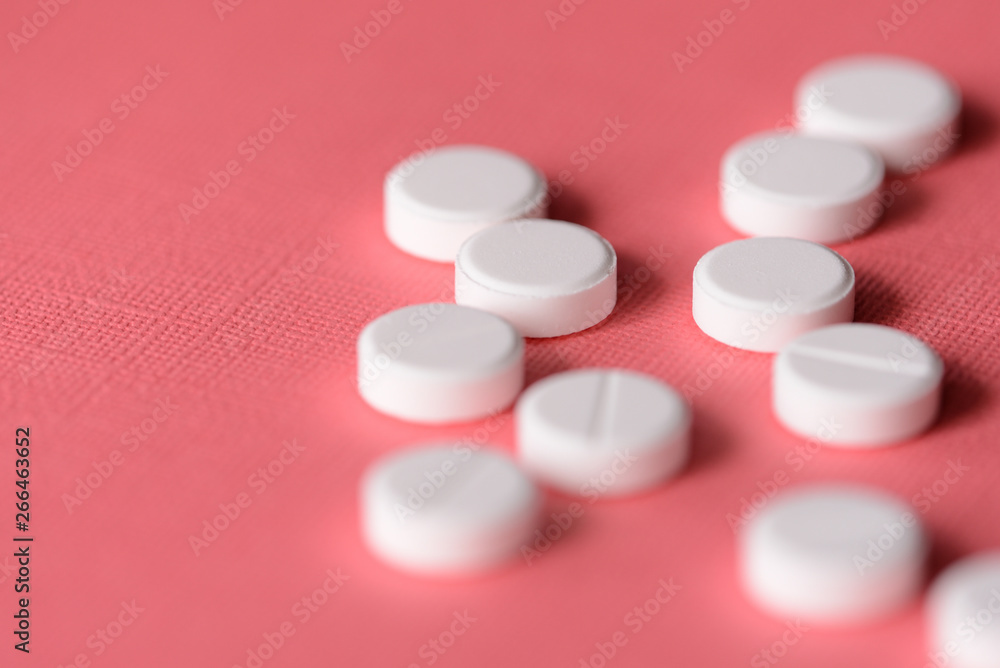 White tablets scattered on a pink background close up White tablets scattered on a pink background close up