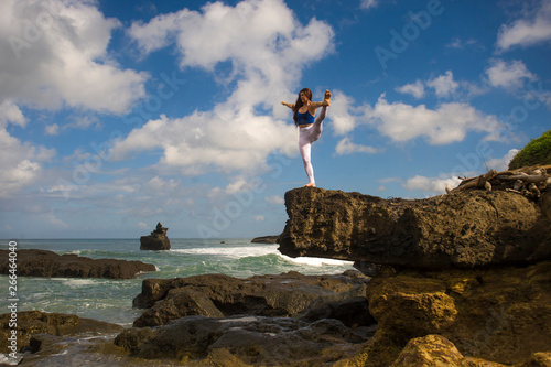 young attractive and concentrated woman practicing acroyoga balance exercise and yoga flexibility and meditation at beautiful beach rock cliff in healthy lifestyle