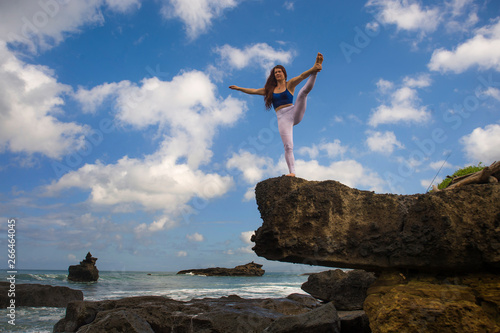 young attractive and concentrated woman practicing acroyoga balance exercise and yoga flexibility and meditation at beautiful beach rock cliff in healthy lifestyle