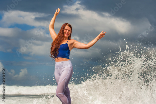 young happy and attractive red hair woman playing excited spreading arms feeling free and relaxed getting wet by sea waves splashing on her enjoying beach
