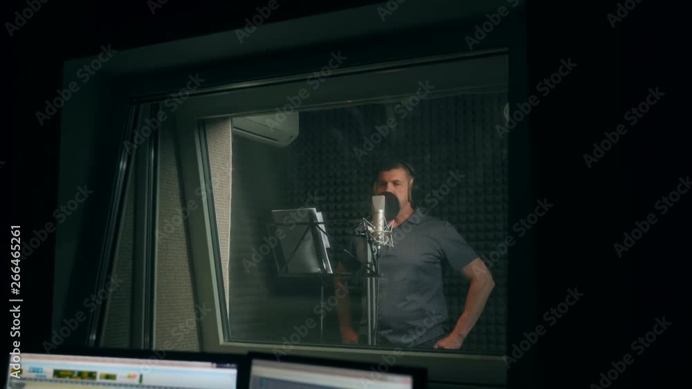 Male singer in headphones singing song into the microphone at sound studio. Show business concept. Adult man recording a song in the studio. Male singer in headphones singing song into the microphone at sound studio. Show business concept. Adult man recording a song in the studio.