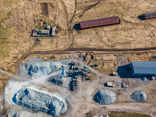 Aerial view of a small plant for the production and cleaning rubble and cement near the heaps of building materials from the pipe of which gray smoke goes, the tractor transports the finished product.